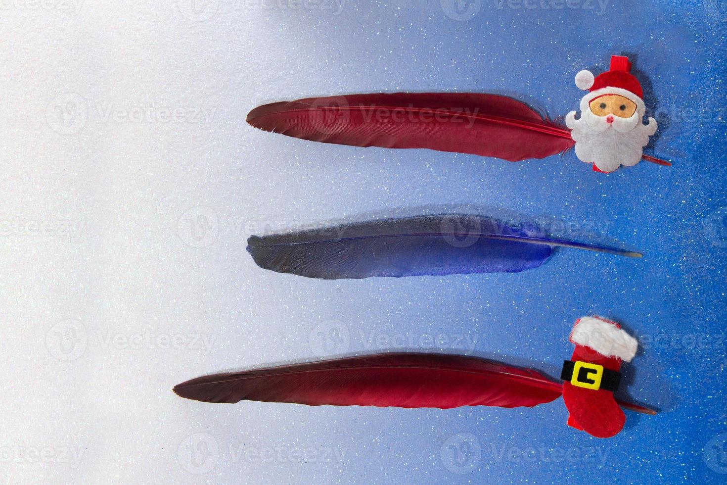 Gold, red, blue, silver feathers with pin with santa claus and a boot on a blue background. For list, write text, planning. Three lines. Christmas and New year photo
