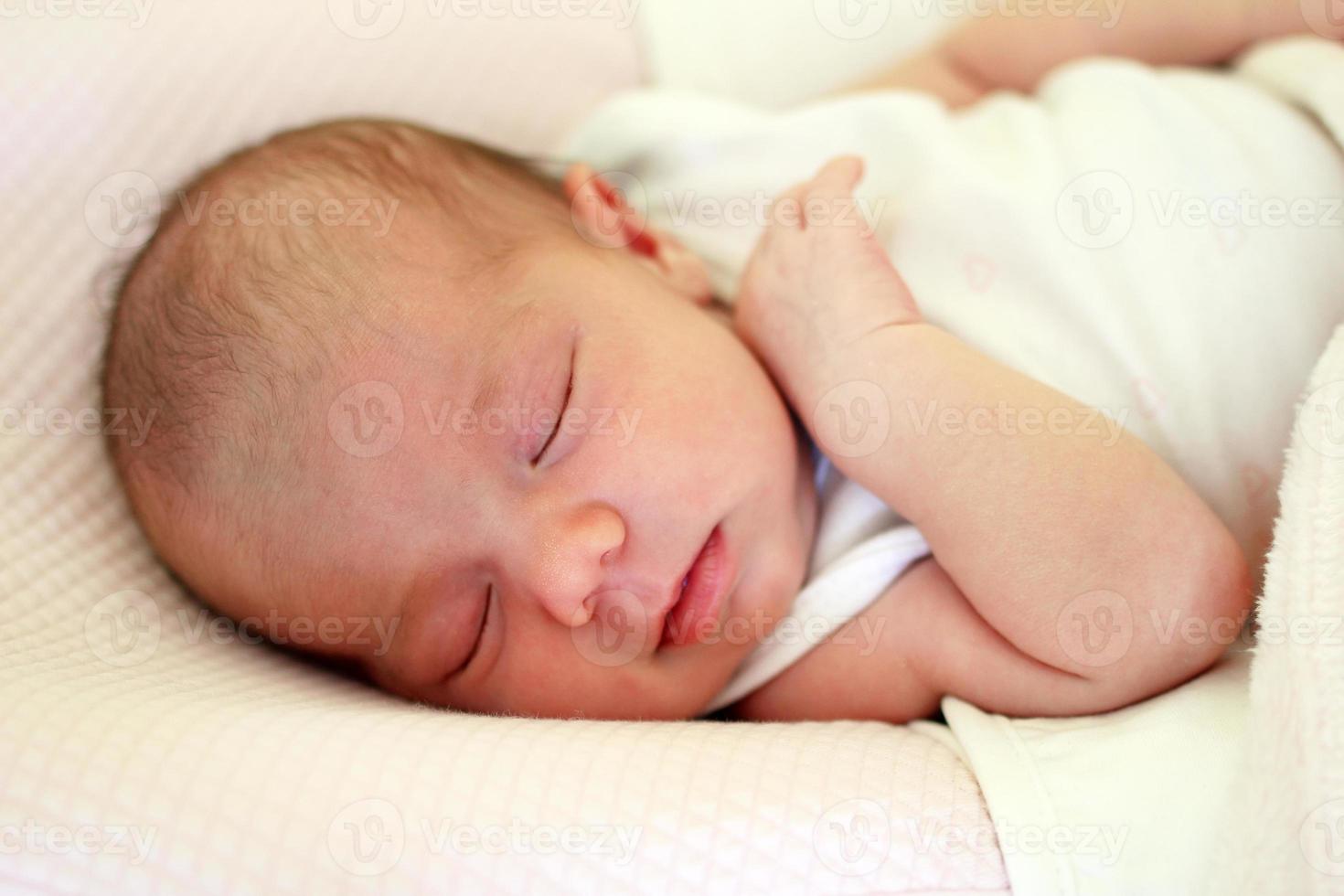 Portrait of cute newborn baby sleeping on a pink bed under beige blanket. photo