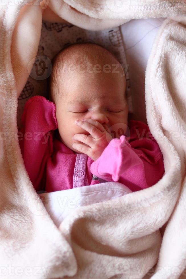 Cute newborn baby in pink baud is sleeping on her bed under beige blanket. photo