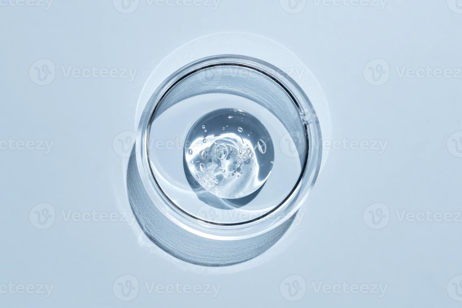 Top view of cosmetics gel with bubbles structure in the petri dish on blue background. ransparent cosmetic liquid or face serum, Transparent cosmetic gel Swatch photo