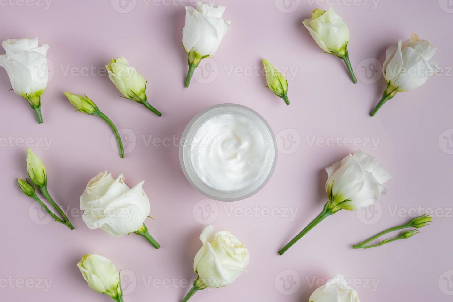 Top view of open jar with face cram surrounded scattered blooming eustoma flowers. Skin care cosmetics presentation. photo