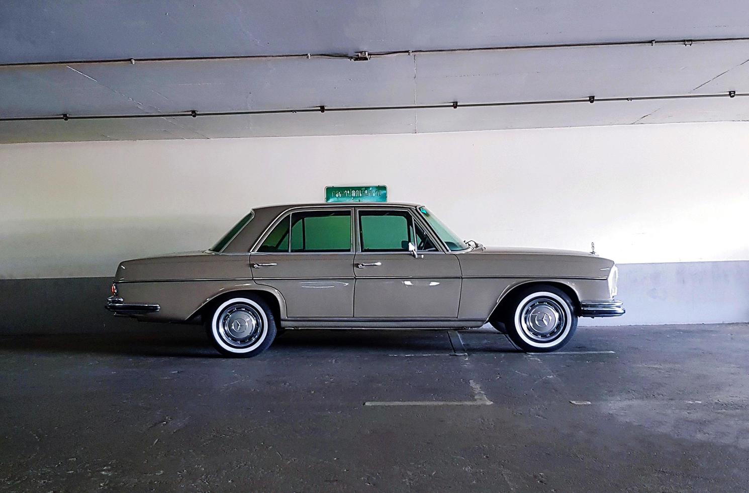 Bangkok, Thailand - June 20, 2022 Brown Mercedes Benz parked in parking with white concrete wall background. Vintage or retro car on street. Classic vehicle on road produces from England and luxury. photo