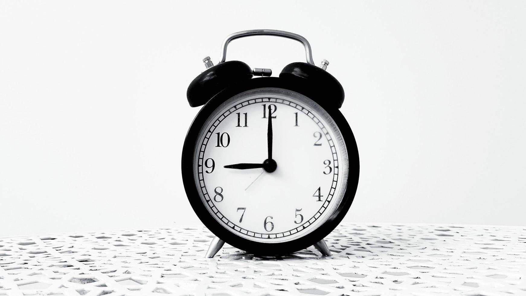 Vintage clock on table isolated on white background in monochrome or black and white tone with copy space. Retro object. 9 o' clock. Morning time photo