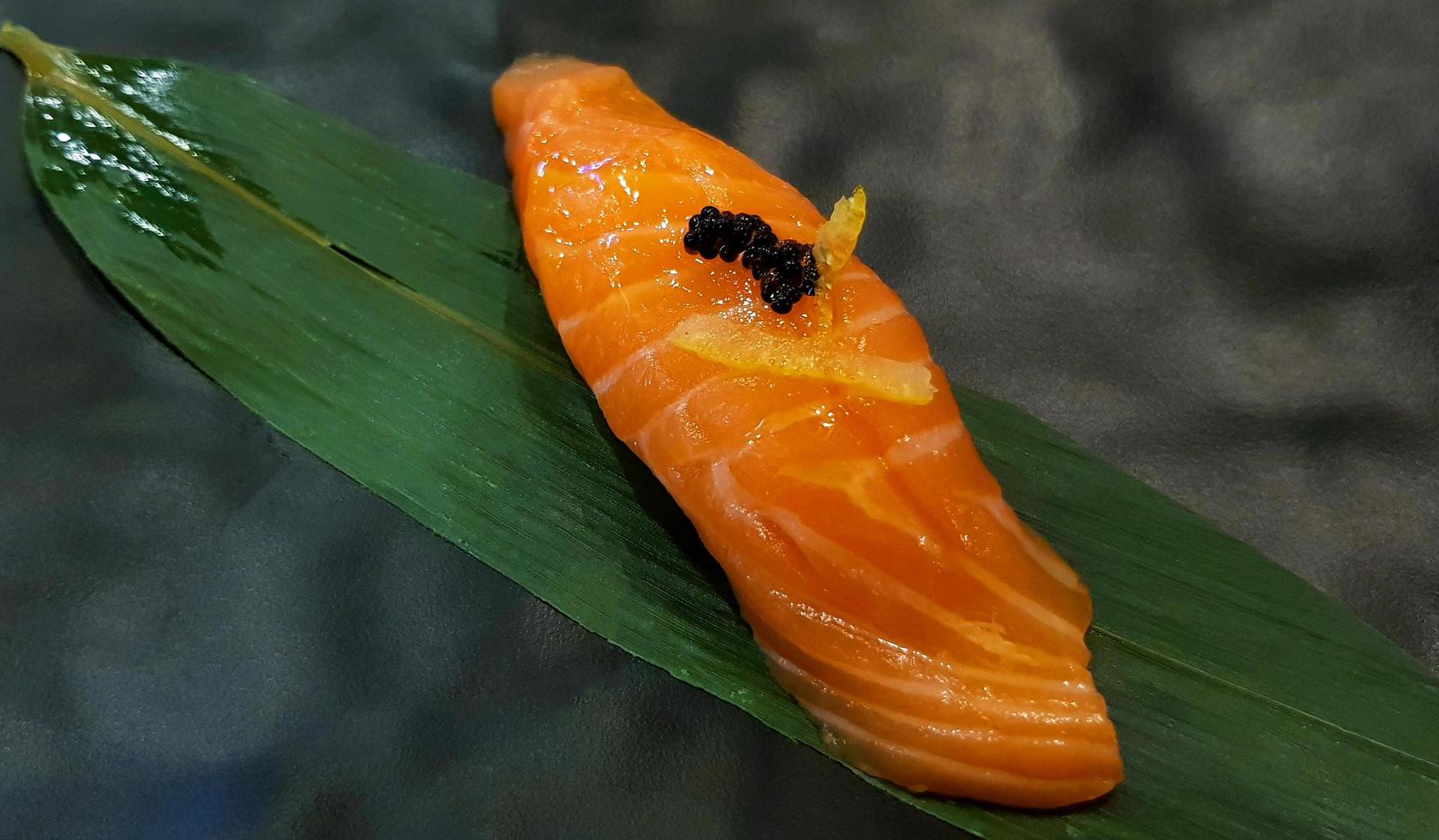 cierra el sushi de salmón fresco en la hoja de bambú verde en el restaurante japonés. comida asiática, delicioso pescado rebanado en arroz japonés con espacio para copiar. concepto de estilo de vida de alimentación saludable. foto