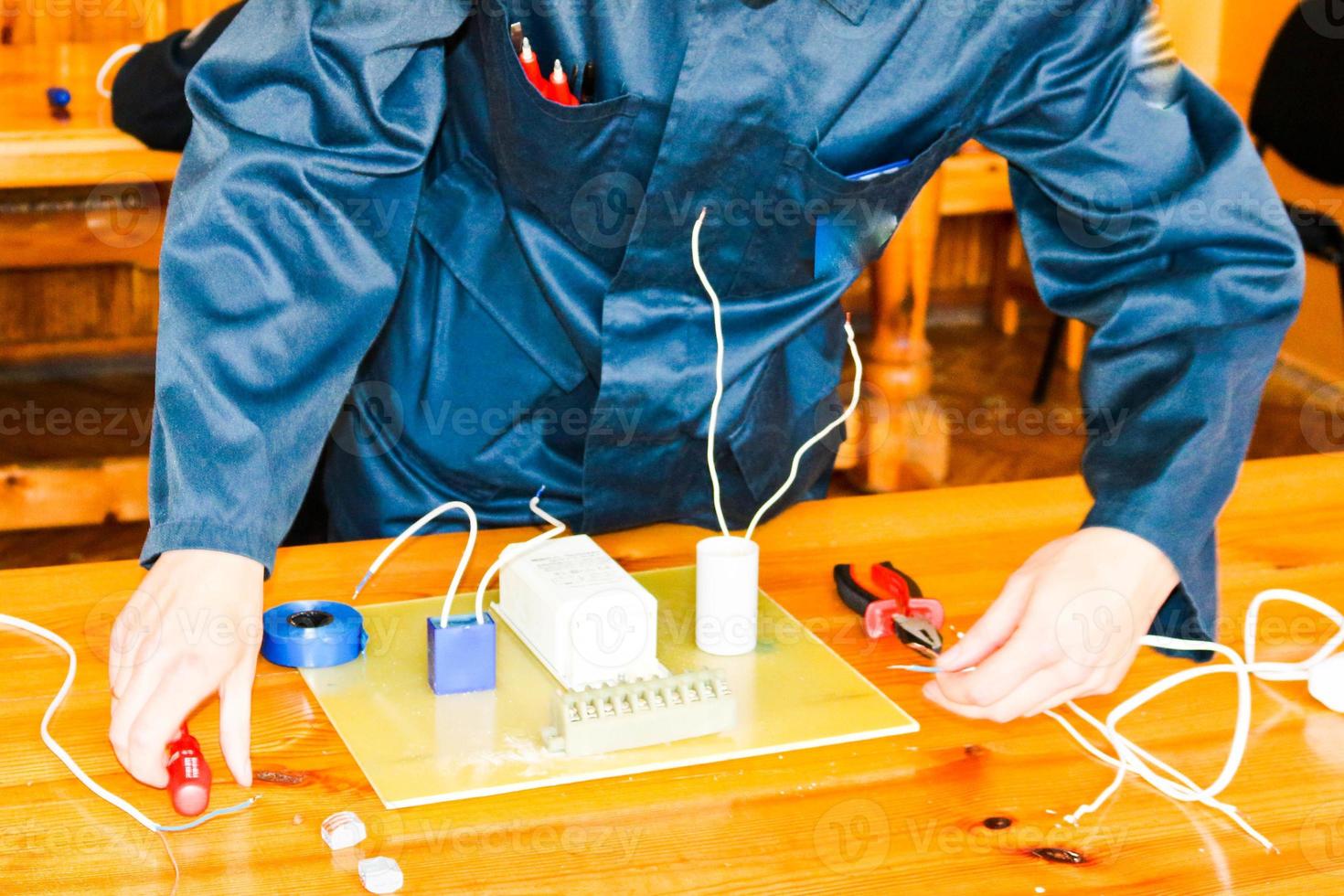 un electricista que trabaja, recoge el circuito eléctrico de una gran farola blanca con cables, un relé en una fábrica de plantas industriales foto