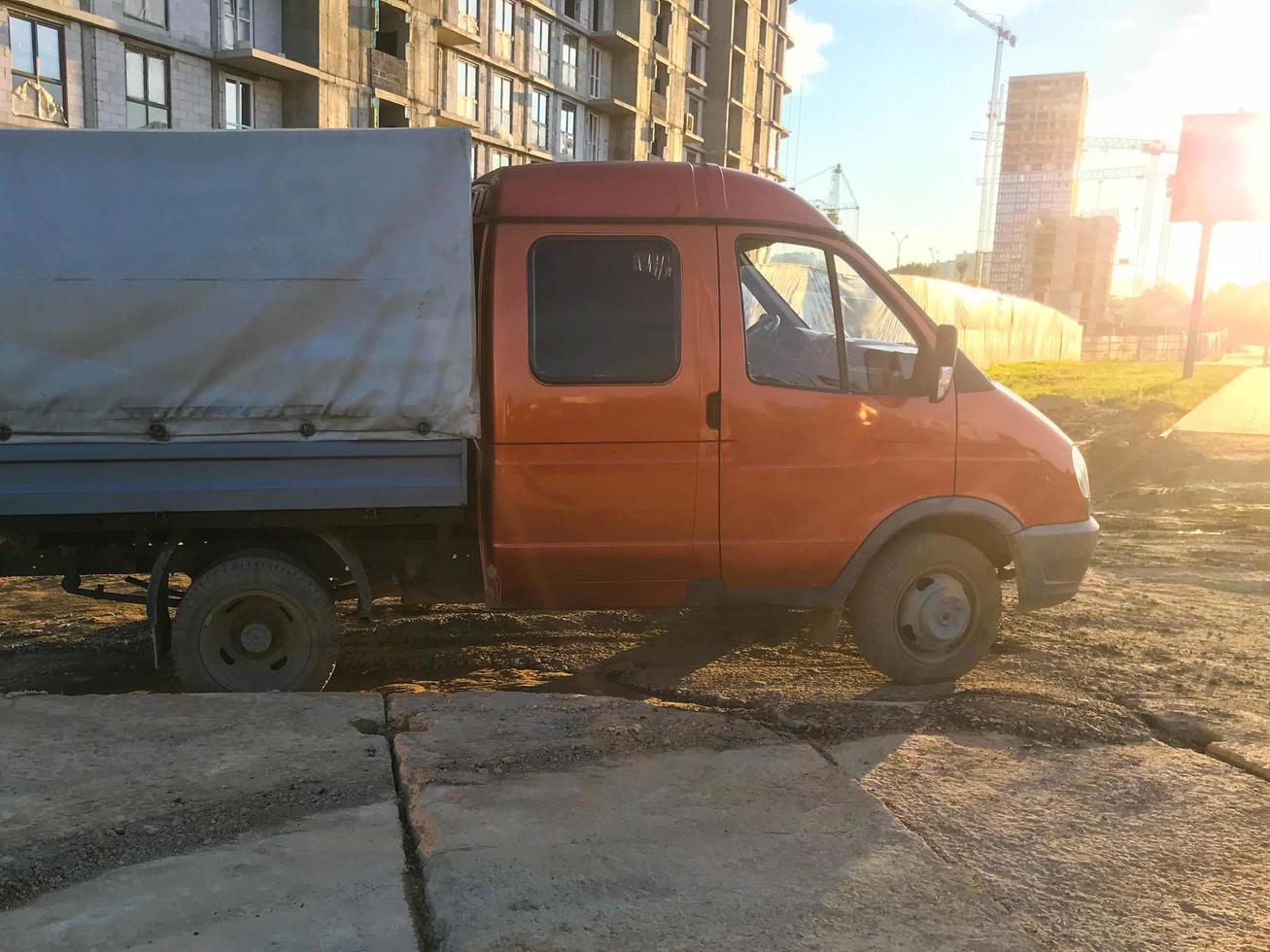 un camión con cabina naranja y base gris se encuentra en el suelo. un coche con ruedas pequeñas para el transporte de mercancías. transporte de materiales de construcción, arena y mercancías foto