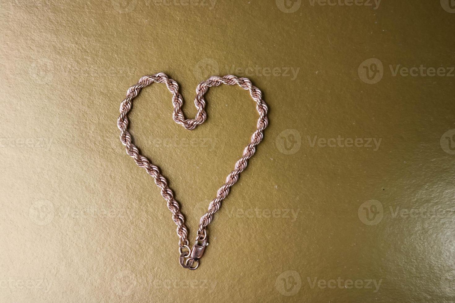 Texture of a beautiful golden festive chain unique weaving in the shape of a heart on a yellow gold background and copy space. Concept love, marriage proposal, marriage, St. Valentine's Day photo