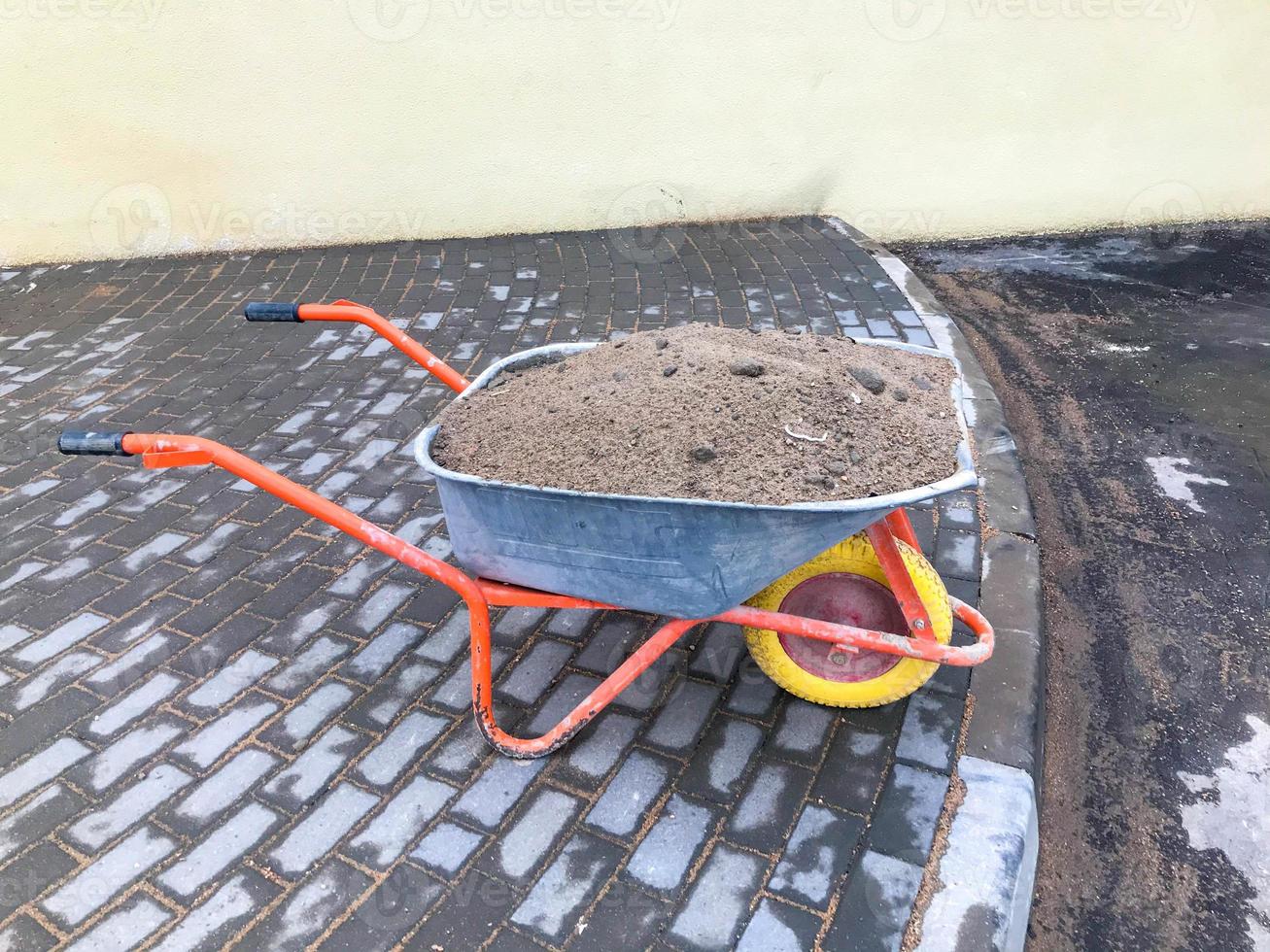 trolley for transporting heavy materials, concrete, bricks and sand. filled with fresh sand for filling holes, building an improved road surface. white stones are visible at the top photo