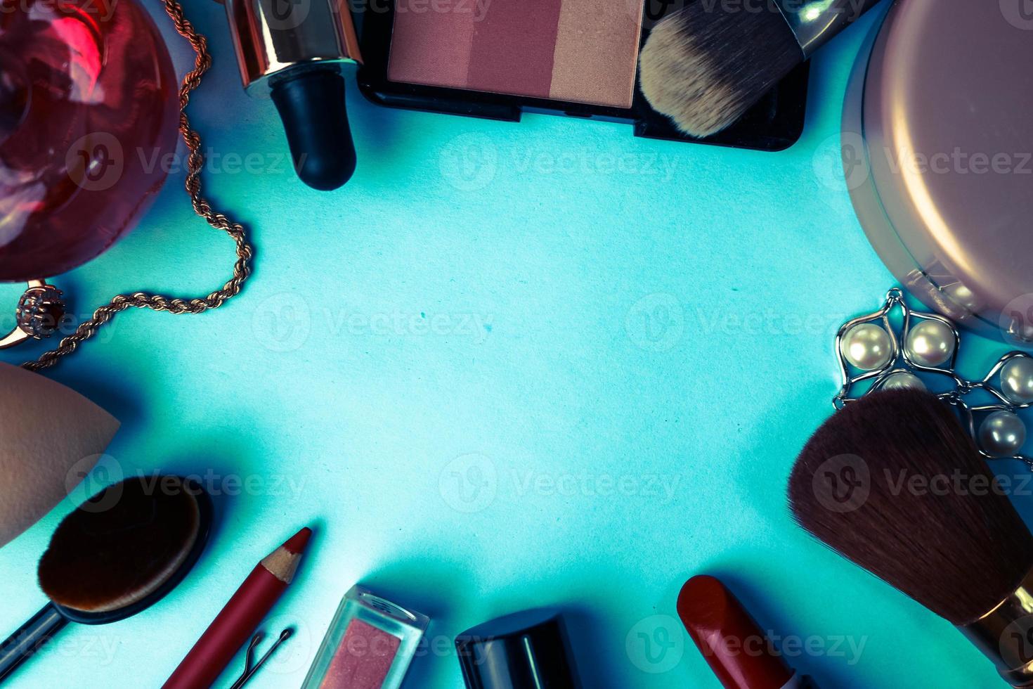 marco de un conjunto de cosméticos femeninos de un lápiz labial, un resaltador, un lápiz para labios, pinceles, pinceles, perfume, polvo, adornos sobre un fondo azul. caja de belleza plana. vista superior foto