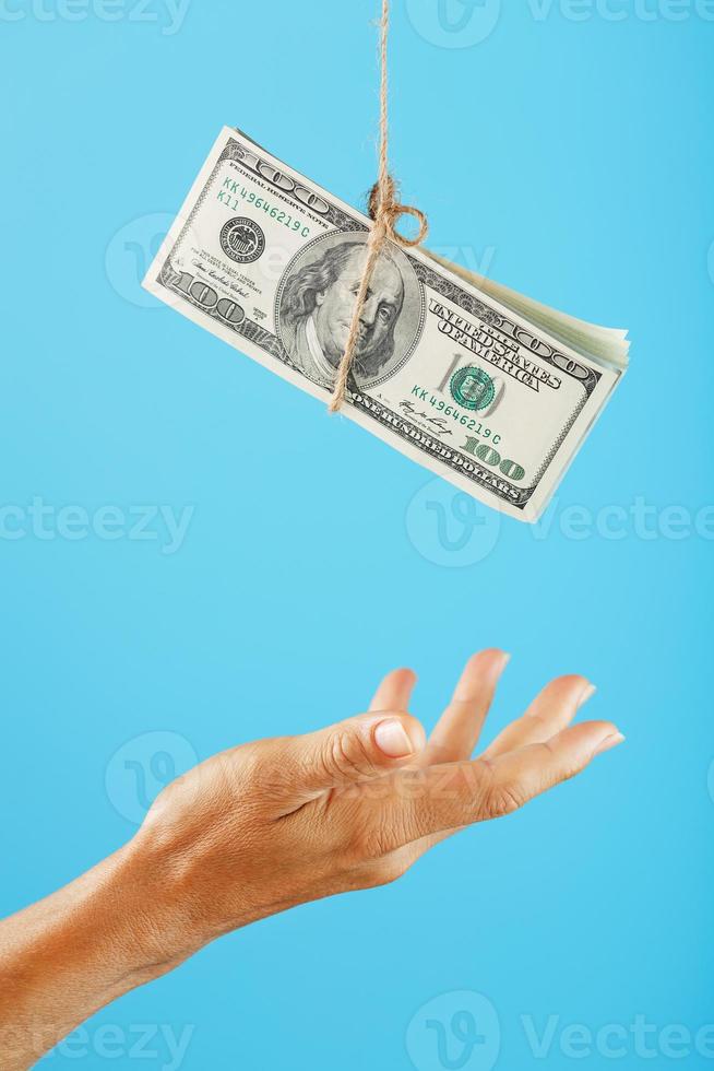 A wad of dollars on a string above a human palm on a blue background. photo