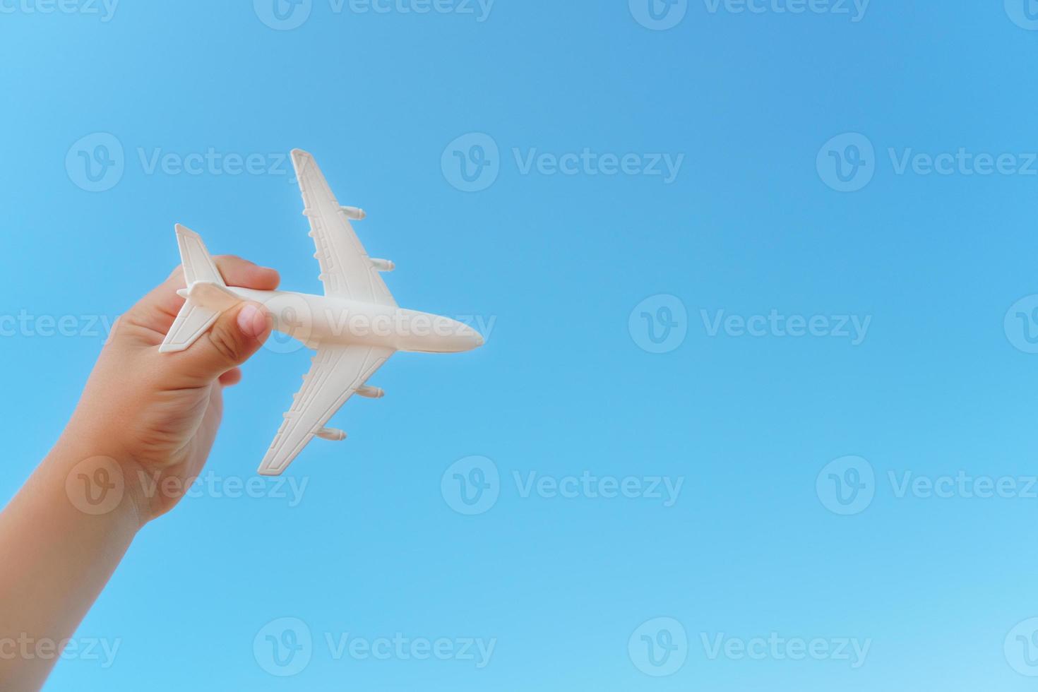 un avión blanco en la mano de un niño contra un cielo azul. el concepto de un sueño de viajes y vuelos. foto