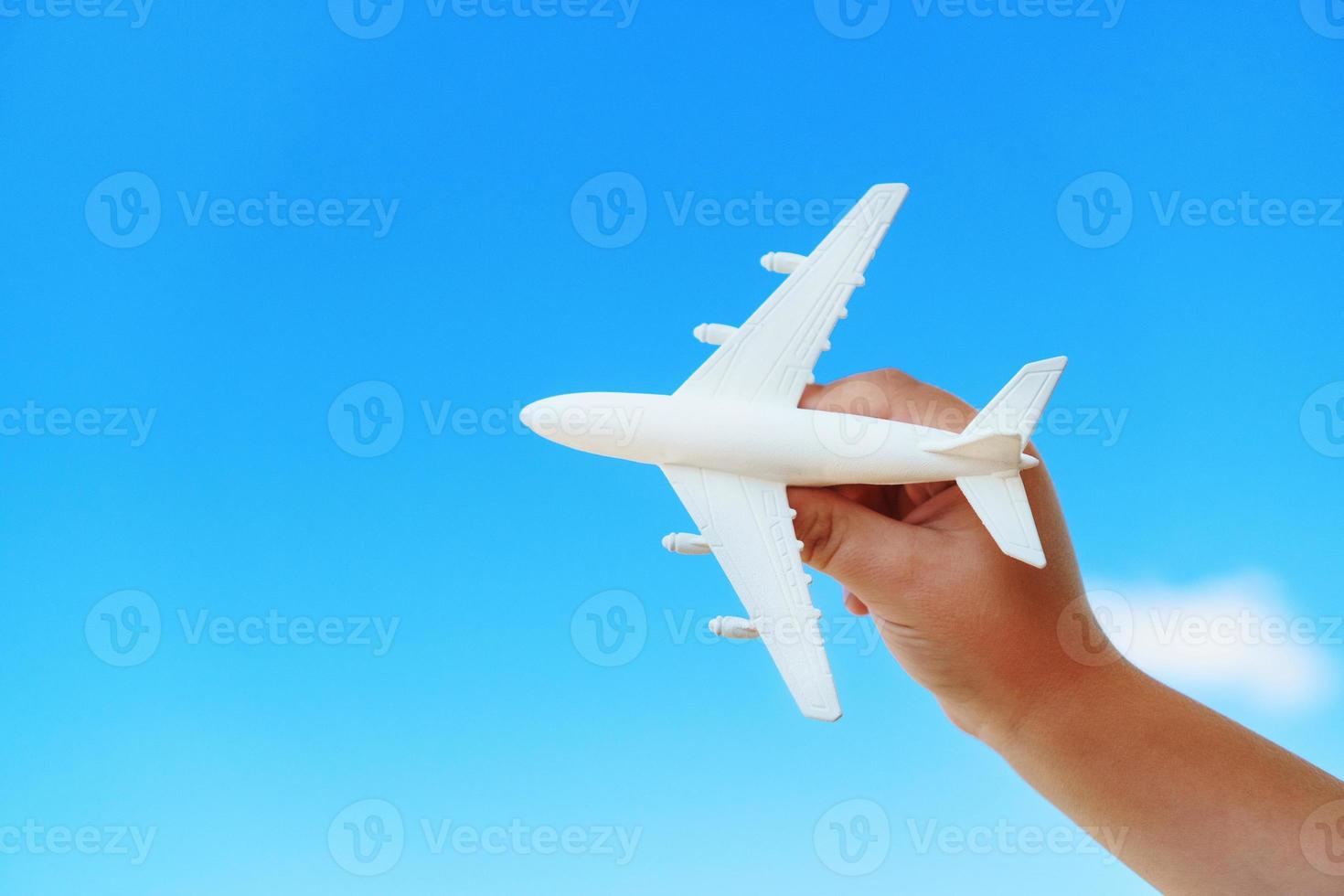 A white toy plane in a child's hand against a blue sky. photo