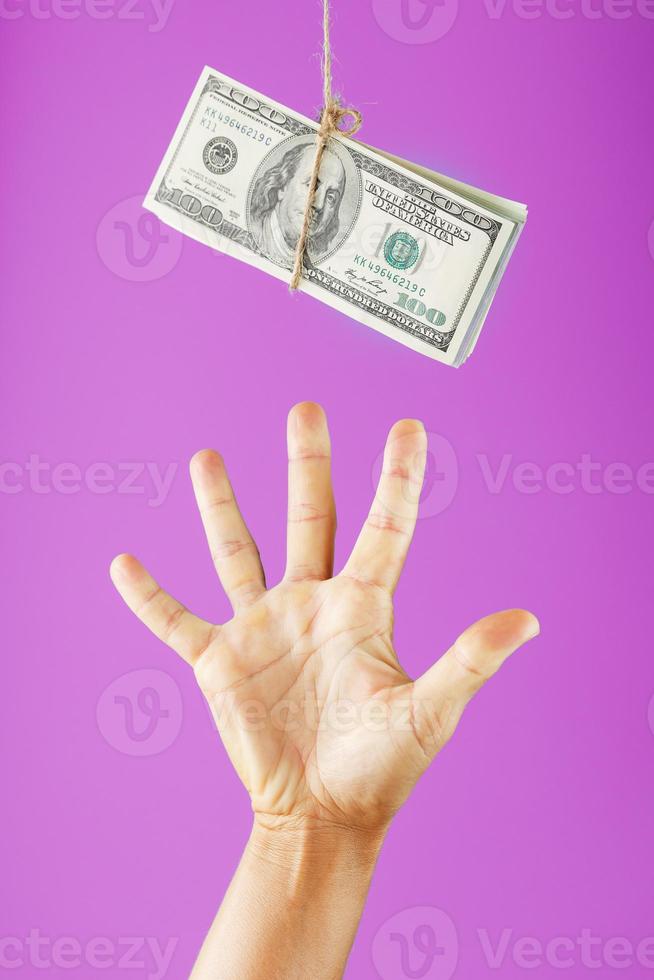 A hand tries to grab the money on a rope on a pink background. photo