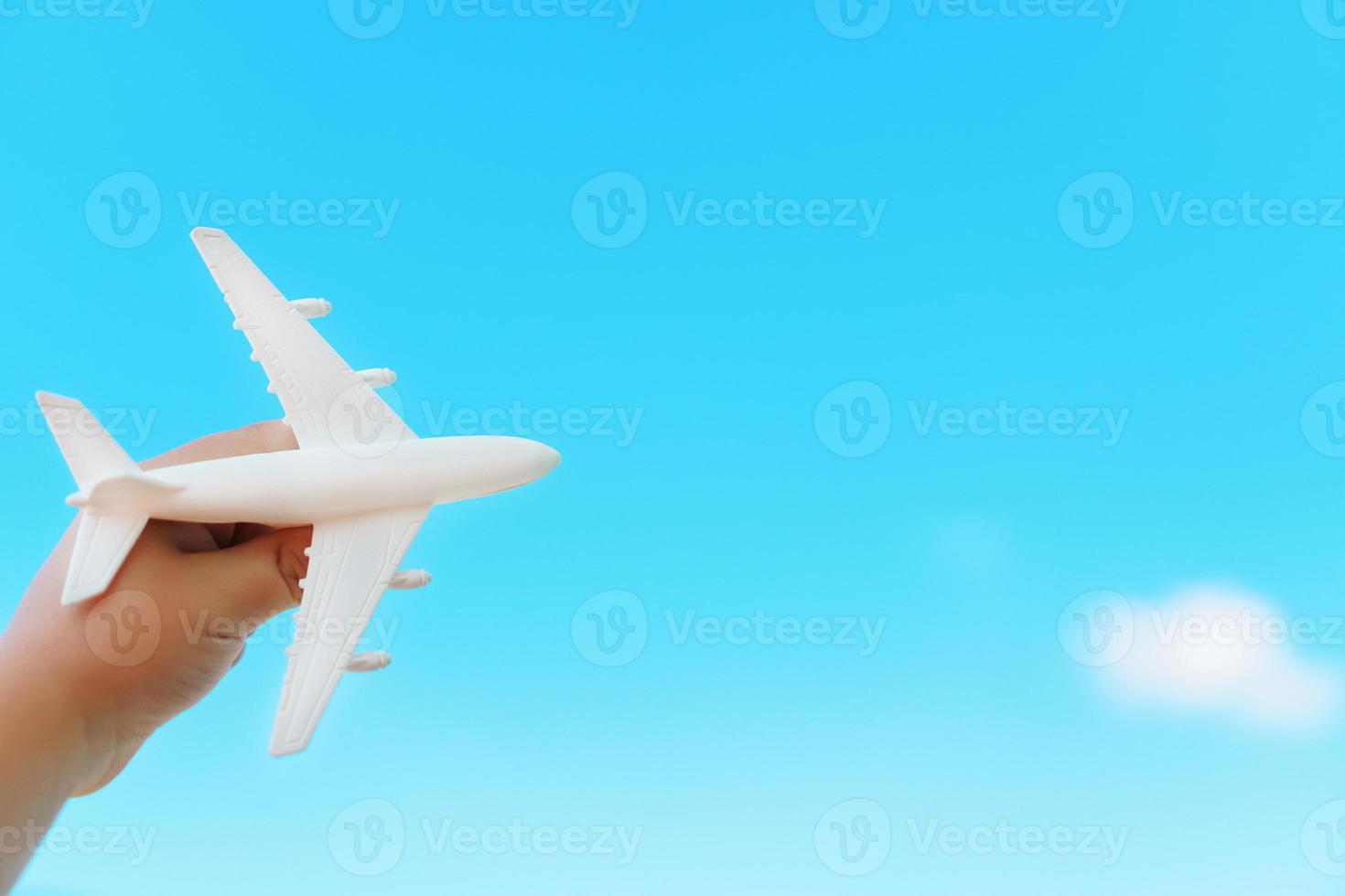 A white airplane in a child's hand against a blue sky. The concept of a dream of travel and flights. photo