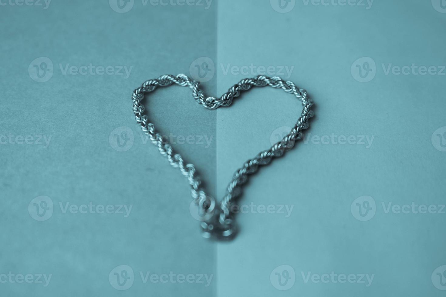 Texture of a beautiful golden dear festive chain of unique weaving in the shape of a heart on a blue background and copy space. Concept love, marriage proposal, marriage, St. Valentine's Day photo