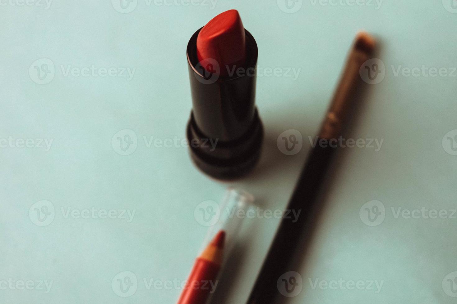 Red fashionable lipour lipad, and highlighter, lip liner and brush on a blue background of a beauty table for makeup for beauty guidance. Flat lay. Top view photo