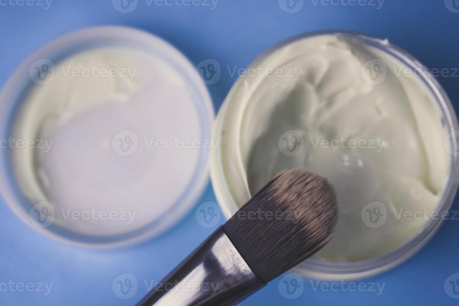 A beauty box with a wooden brush made from natural hard lint for a tone and a round jar of cream, a make-up base with a second skin effect on a blue background. Flat lay. Top view photo