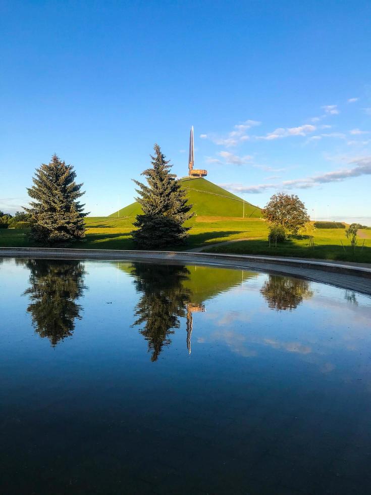 montículo de gloria, complejo conmemorativo. un monumento a la segunda guerra mundial. montículo se refleja en el agua. cerro de tierra, bayonetas de metal para la memoria de los muertos. bielorrusia, minsk, 8 de agosto de 2020 foto