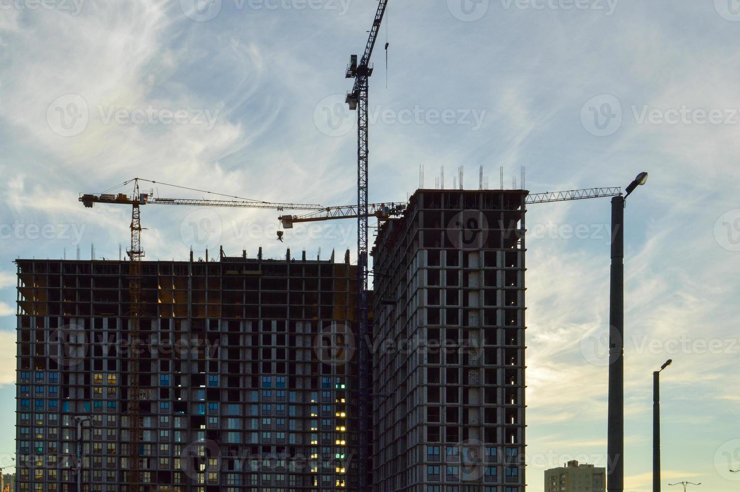 a concrete multi-storey building is being built in the city center. the builders have inserted many windows, the house stands next to lampposts and a construction crane. construction of a new area photo