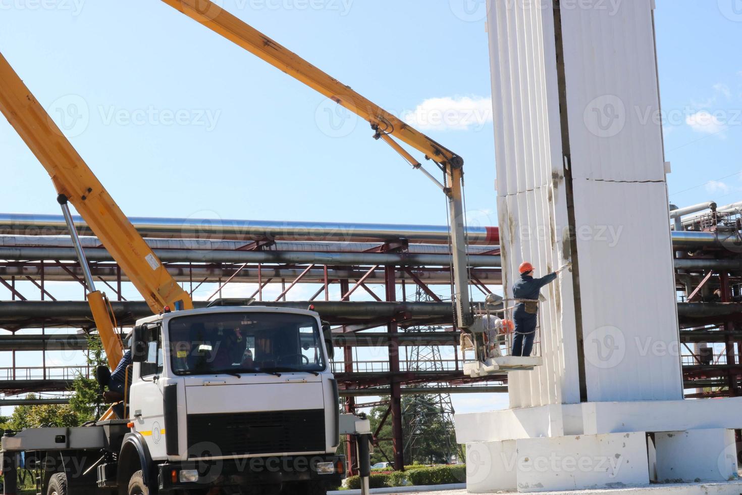 Repair columns on a special technique. Workers on the crane repair a large white column. Cosmetic repair with painting. Workers in a special form paint a column photo