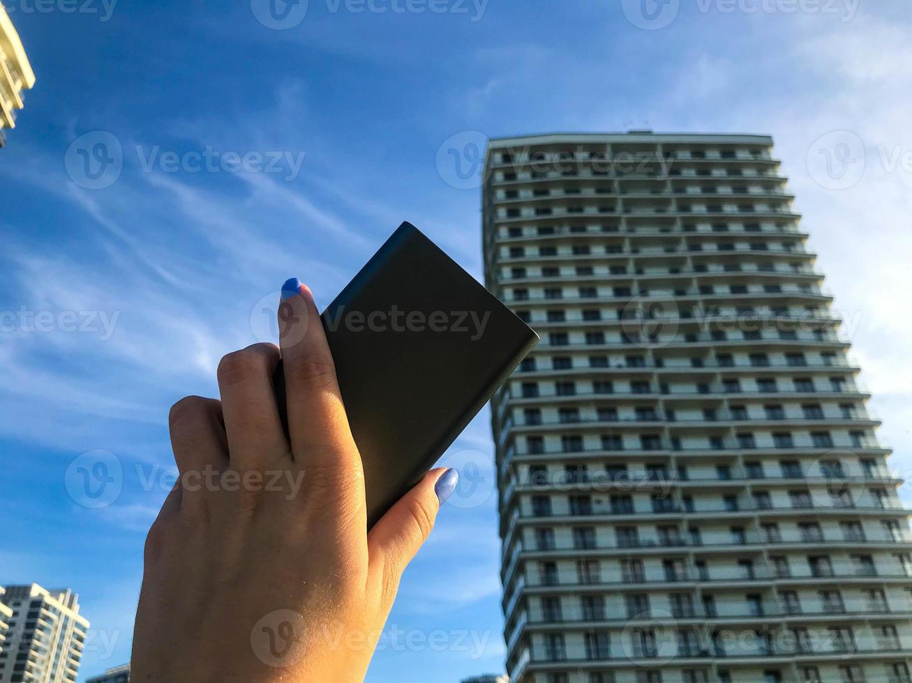 a girl holding a charging block against the background of a high multi-storey residential building. the building is in Arabic style with terraces. the girl has a blue manicure photo
