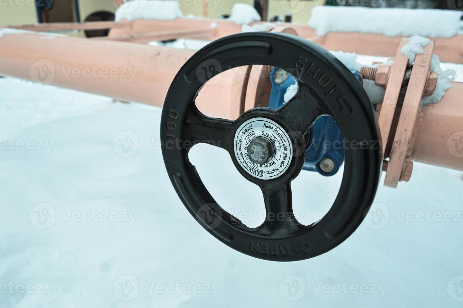 Industrial shut-off regulating protective pipe fittings. Black valve for opening, closing on an iron orange metal pipe with flanges, studs, nuts against the background of white snow in winter photo