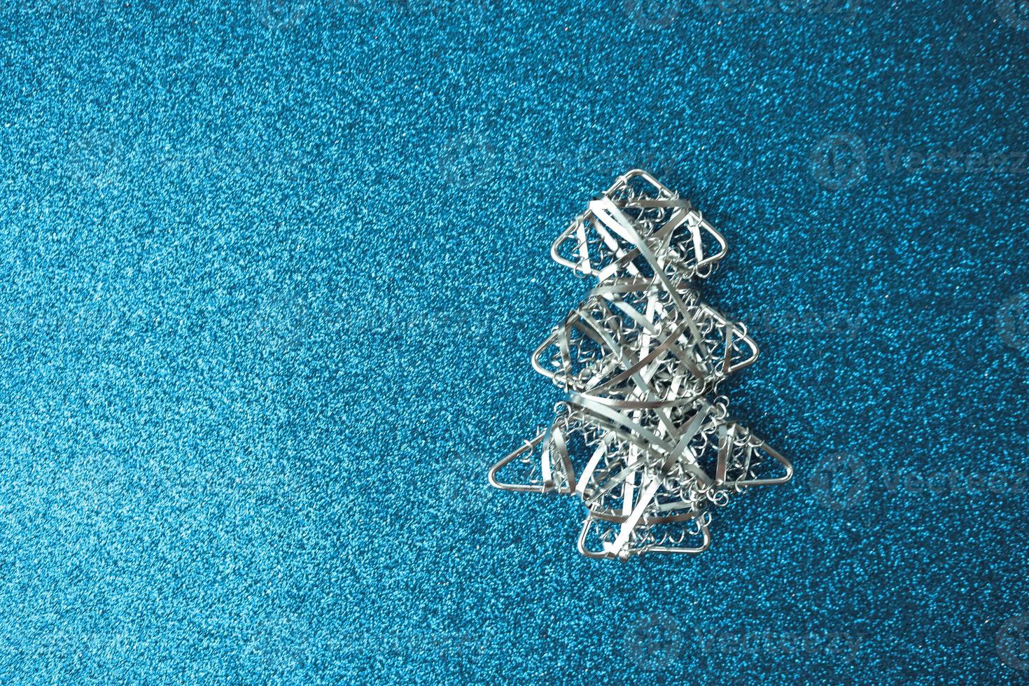 Festive New Year Christmas happy blue shiny joyful background with a small toy metal iron silver homemade Christmas tree. Flat lay. Top view. Holiday decorations photo