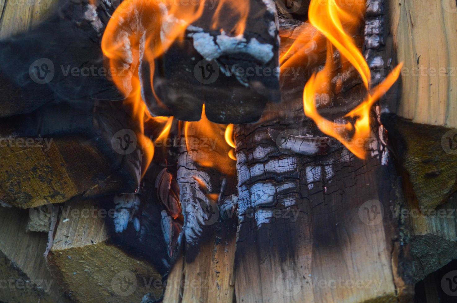 tablones de madera quemados calientes carbonizados de troncos de madera en un fuego con lenguas de fuego y humo. textura, fondo foto