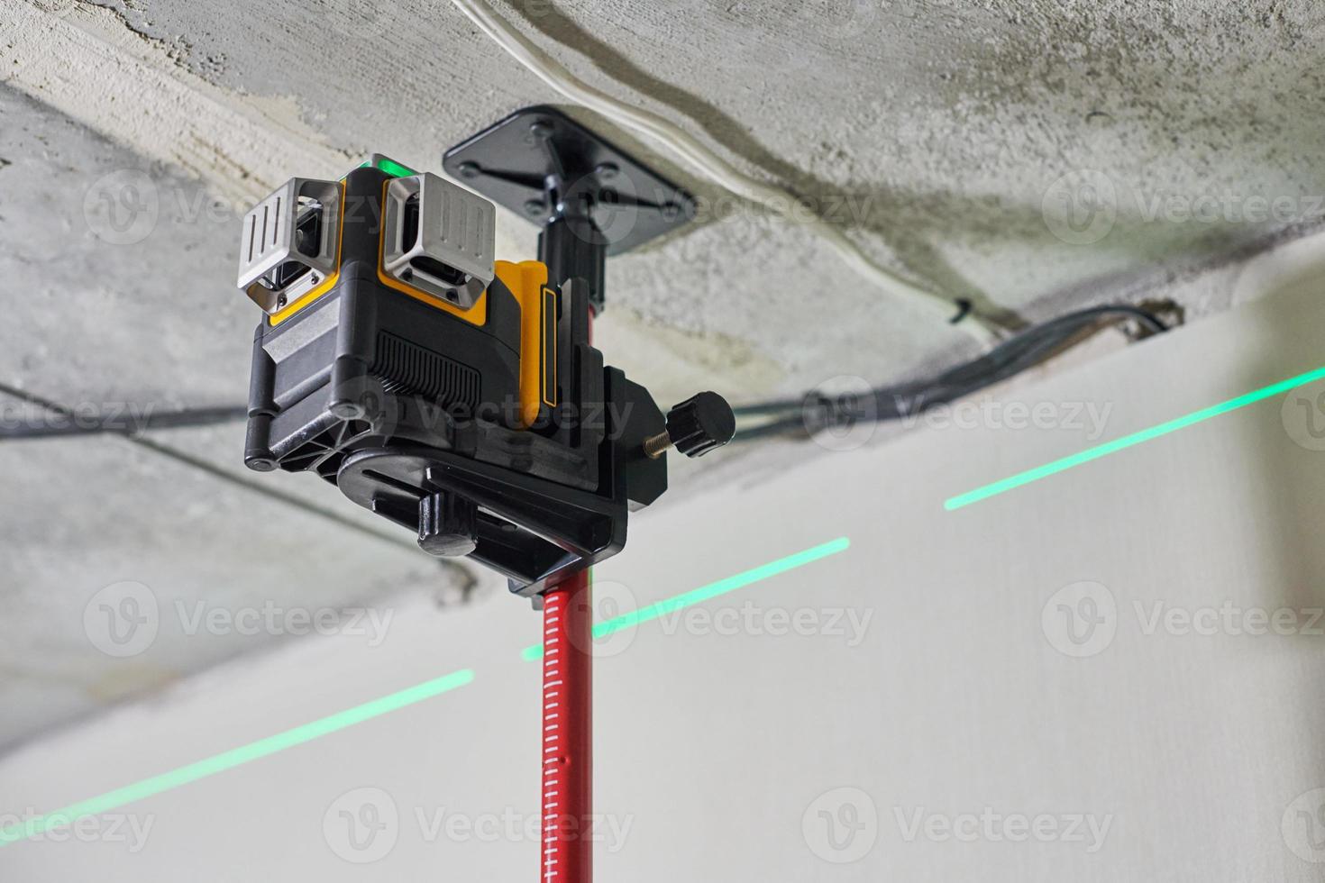 Laser level measuring tool with visible green laser beam on wall for installing stretch ceiling photo