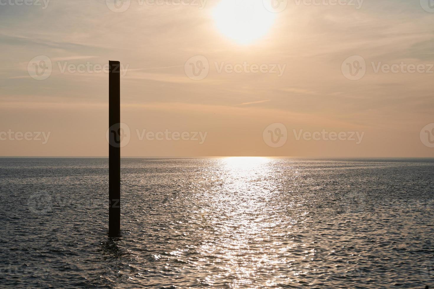 Large rusty steel construction pillar in blue sea with calm waves at sunset, abandoned building part photo