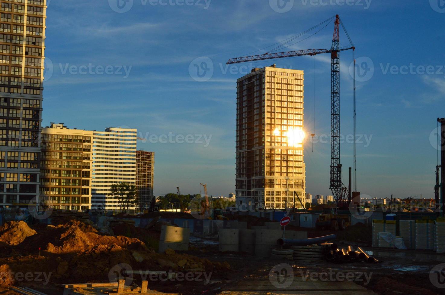 construction of new high houses. a glare of the sun is visible in the window. cranes stacking blocks to build a new floor.  building materials under the film. skyscrapers in the city center photo