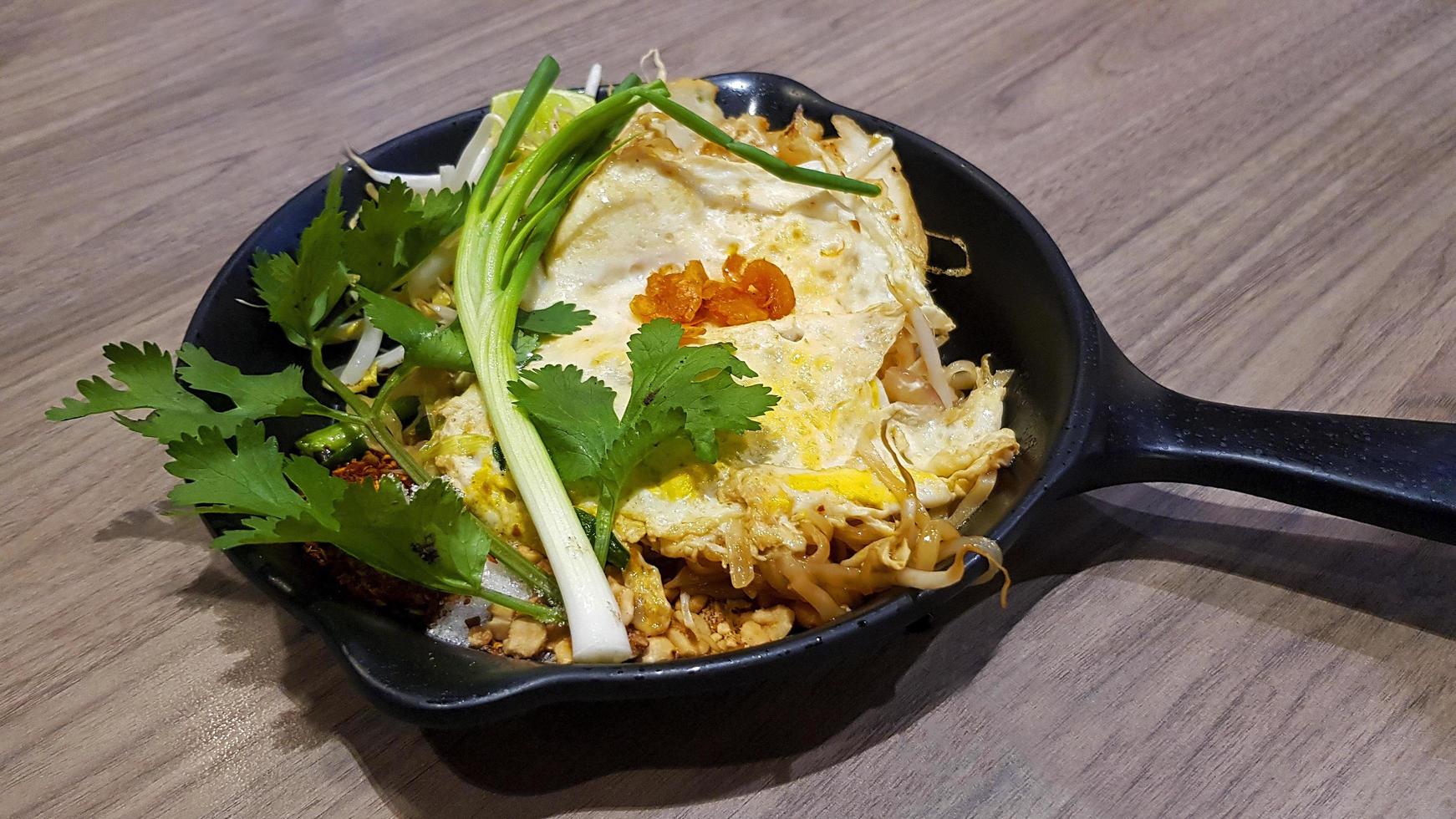 fideos fritos al estilo tailandés con gambas y verduras en sartén caliente sobre fondo de madera o mesa en el restaurante. los asiáticos llaman a este pad de comida tailandés y famoso en Tailandia. deliciosa comida foto