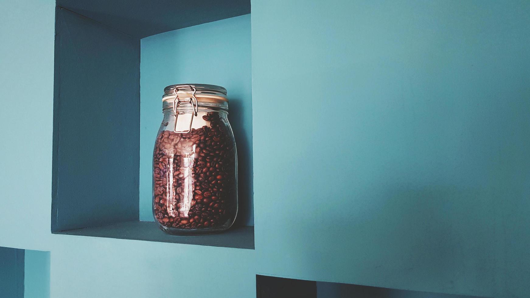 Glass bottle of coffee seed putting on green wooden self and wall background for sale or decorated at caf shop in vintage tone with copy space on right. photo