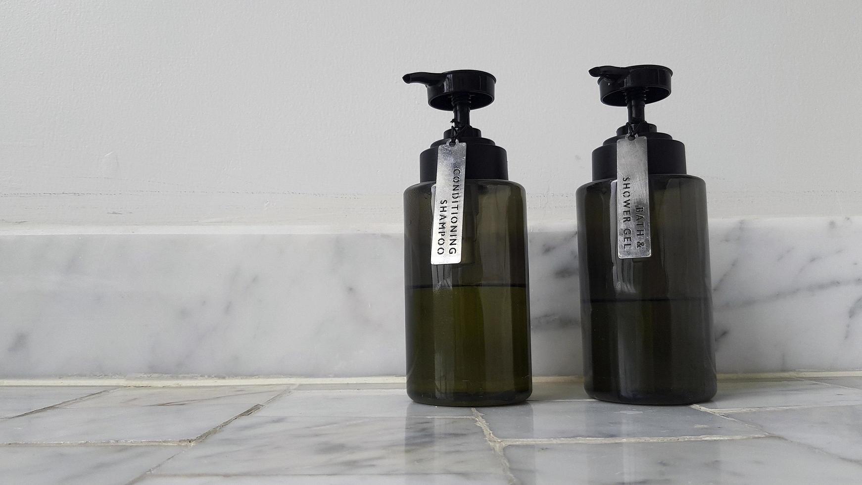 Two black plastic conditioner shampoo and bath shower gel putting on marble floor with white cement wall background with copy space on right. Cleaning part of body and Spa concept photo
