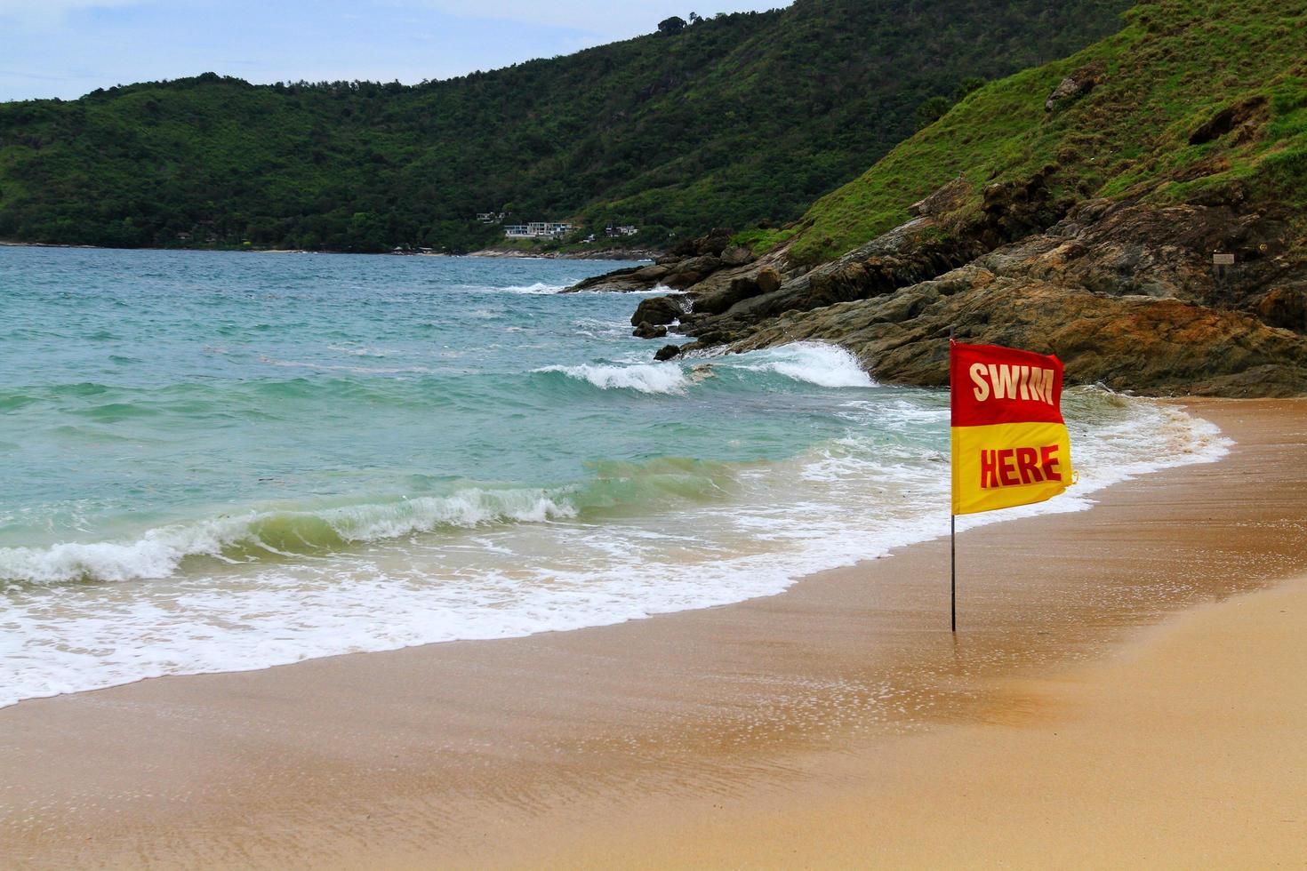 Red with yellow swim hear flag on the beach and sea to tell or inform traveler , tourist and people can swimming in this area at Phuket, Thailand. Seascape with wave, sky and mountain background. photo