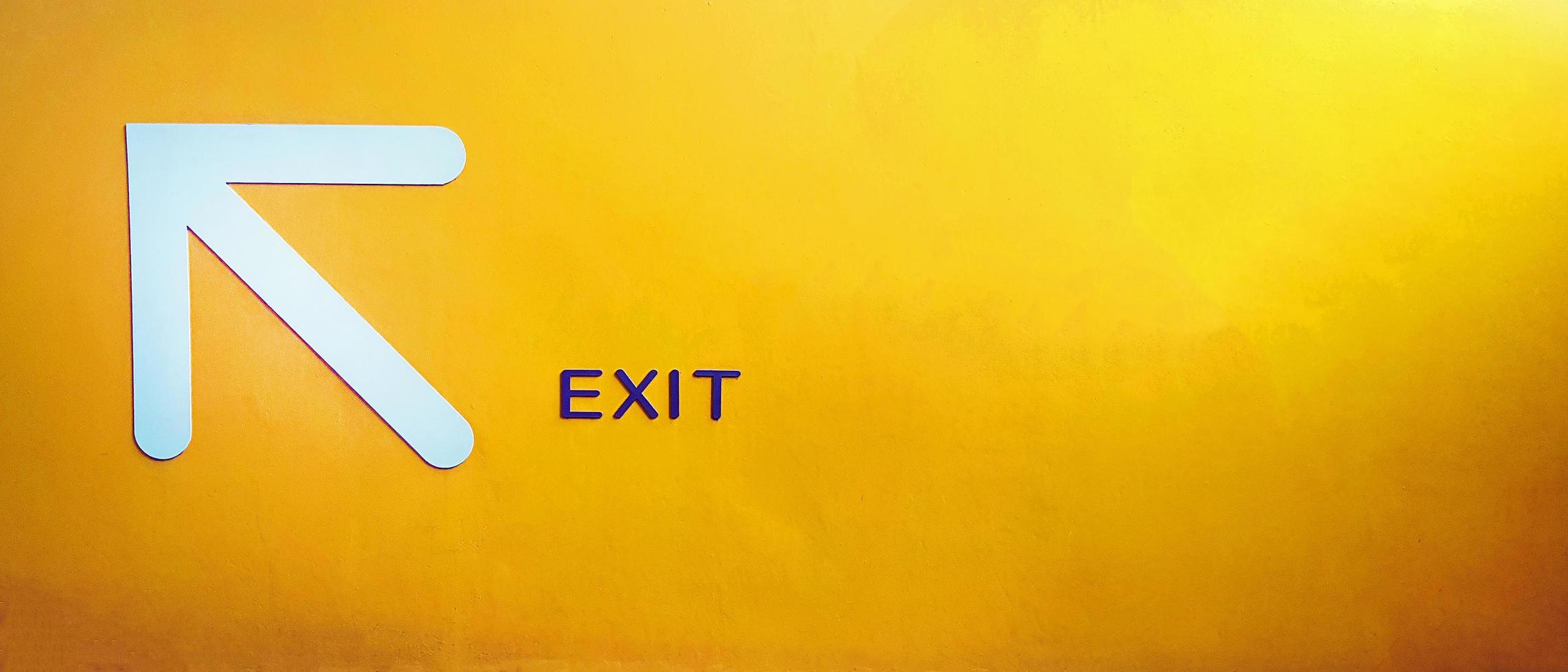 White arrow sign give direction to go up, entrance, exit or way on yellow concrete wall with copy space. Traffic symbol for tell car or people on, street, road or in building on painted background. photo