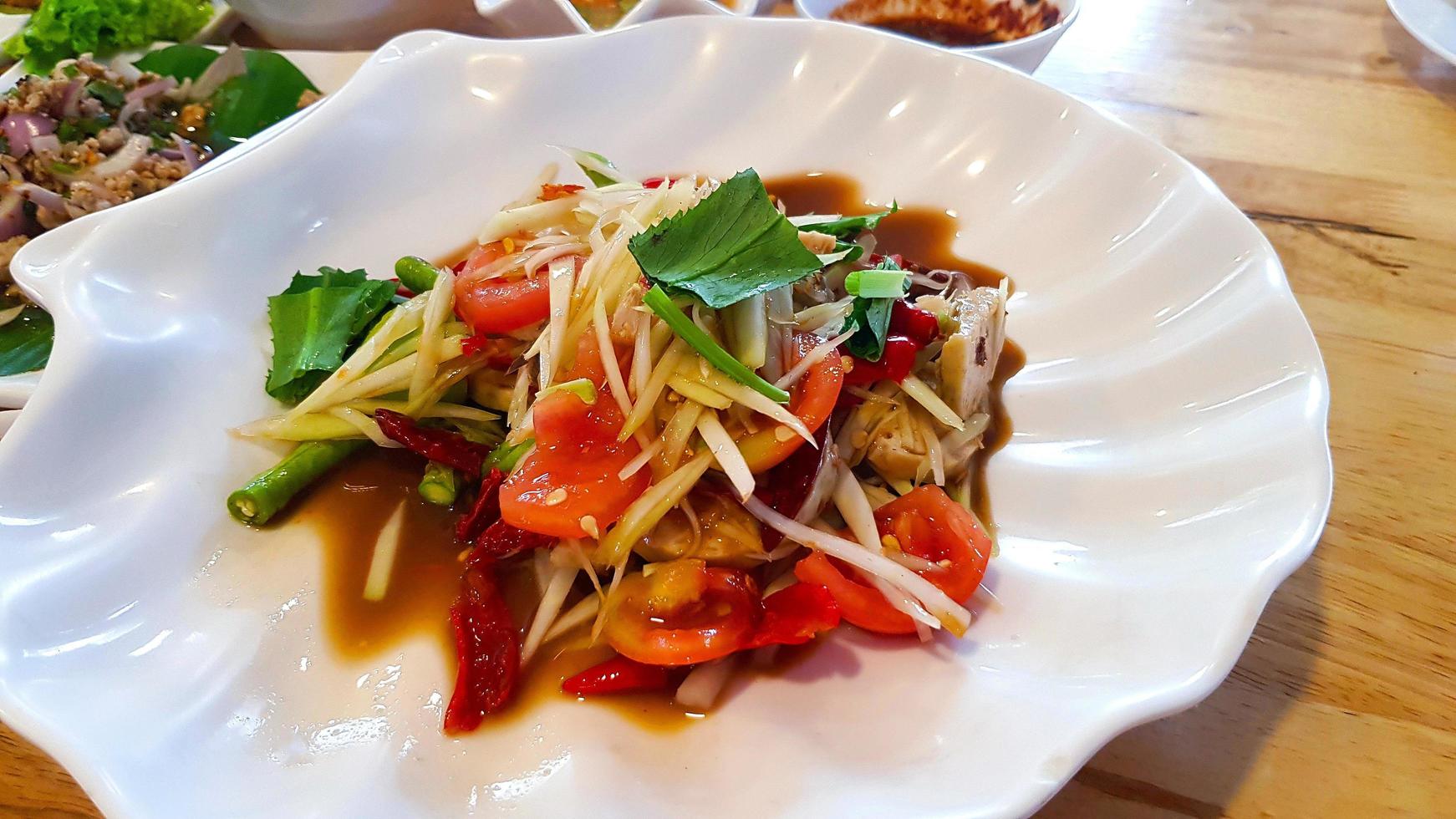 Close up Thai spicy papaya salad with tomato, chili, green bean or nut and sausage on white dish or plate. Famous food in Thailand and Delicious meal. Healthy eating life style and Low fat food. photo