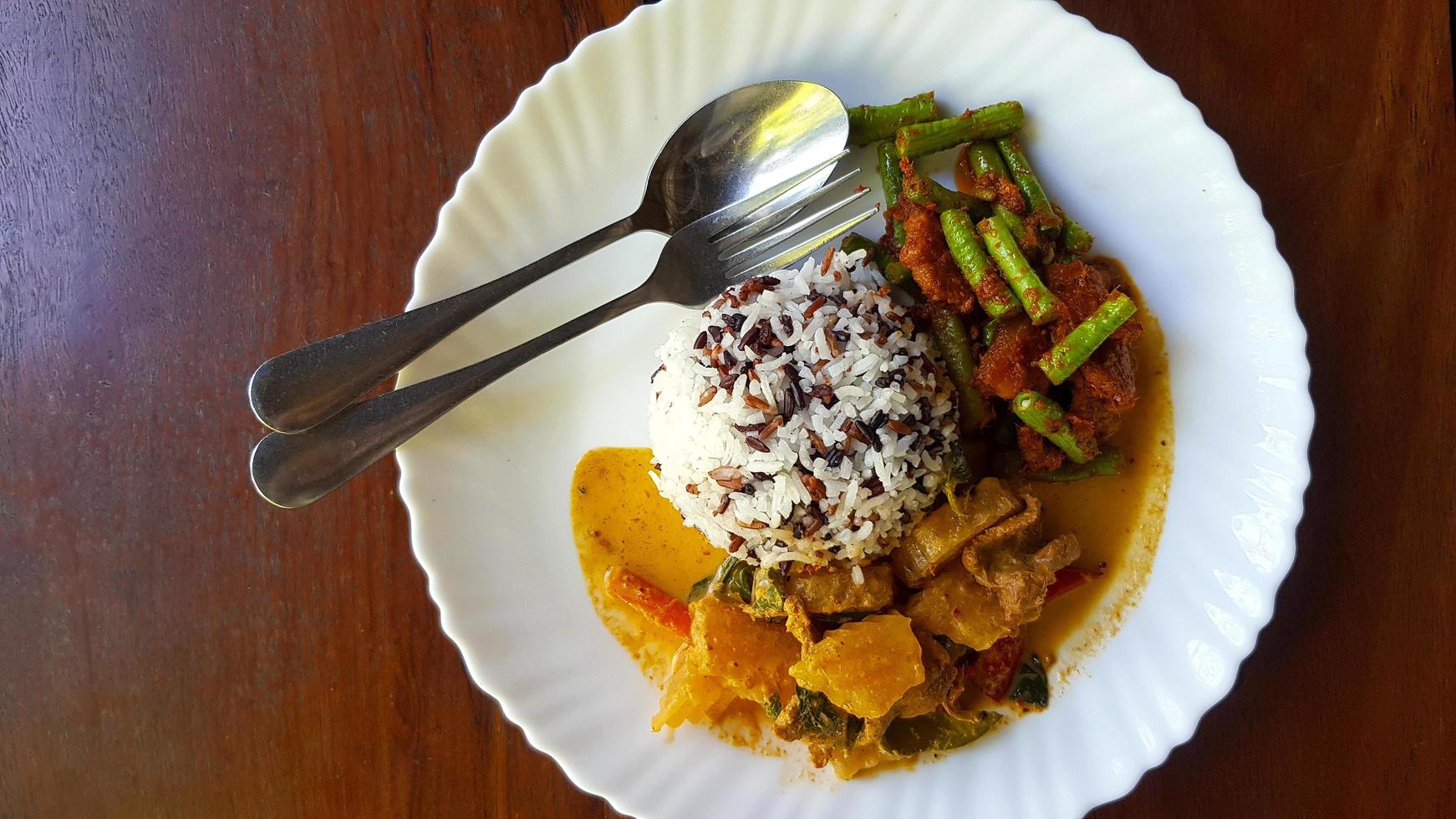 Top view of Three color rice with spicy yellow curry with pork and Stir fried pork belly and red curry paste with string bean in white dish on brown wooden background or table with copy space. photo