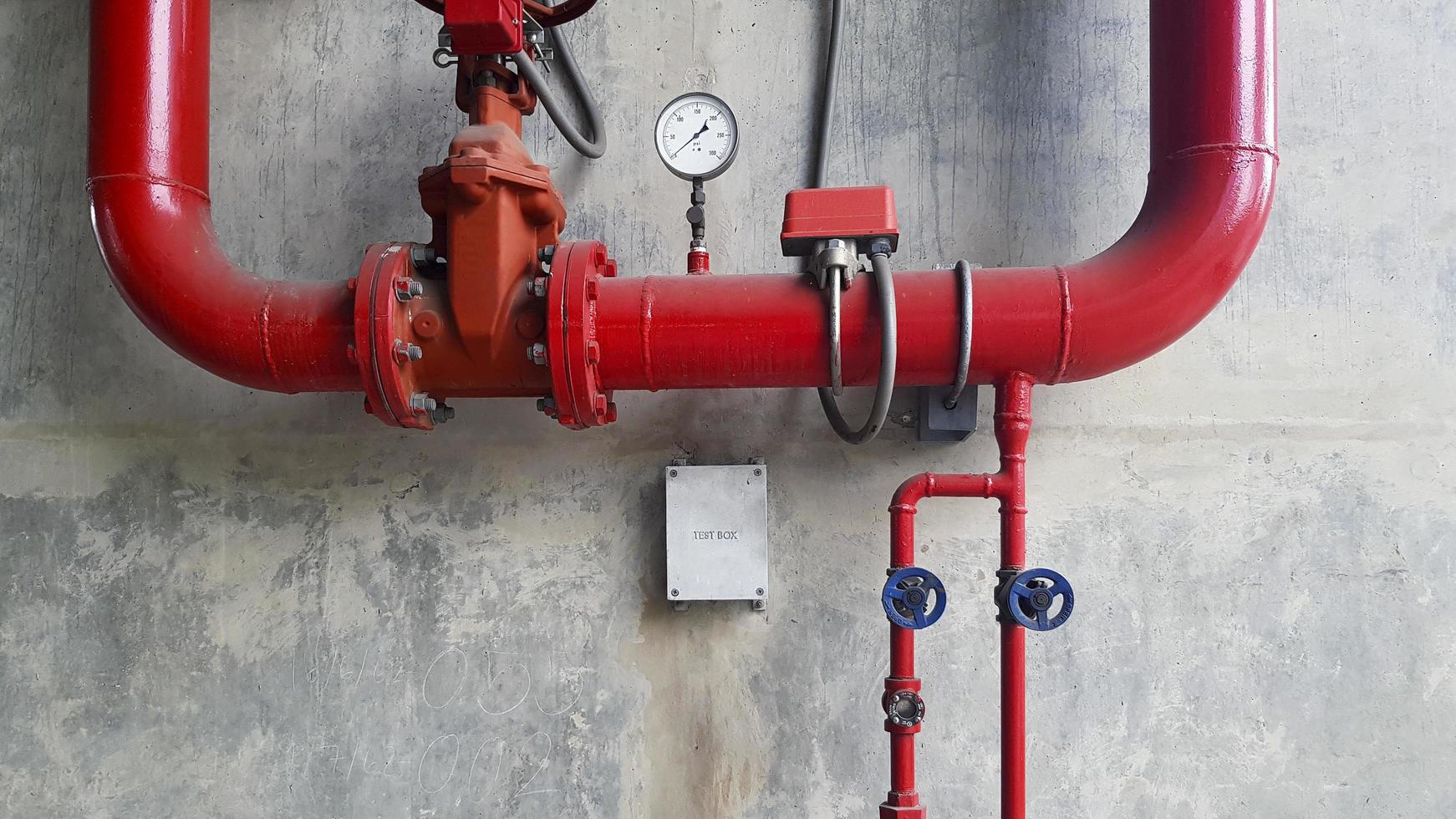 Red water or gas pipeline with gate pressure valve and stainless steel test box installed on concrete wall with copy space. Line pipe industrial and extinguisher pump. photo