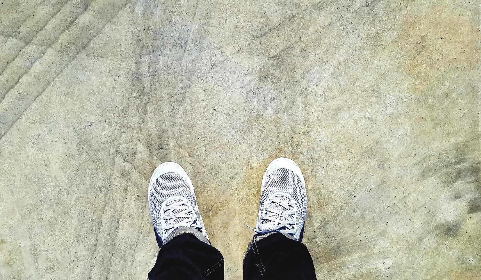 Top view of leg wearing blue jeans and gray or grey sneakers or fashion shoes on floor with car wheel or brake mark on road or street with copy space. Flat lay of part body. Abstract background photo