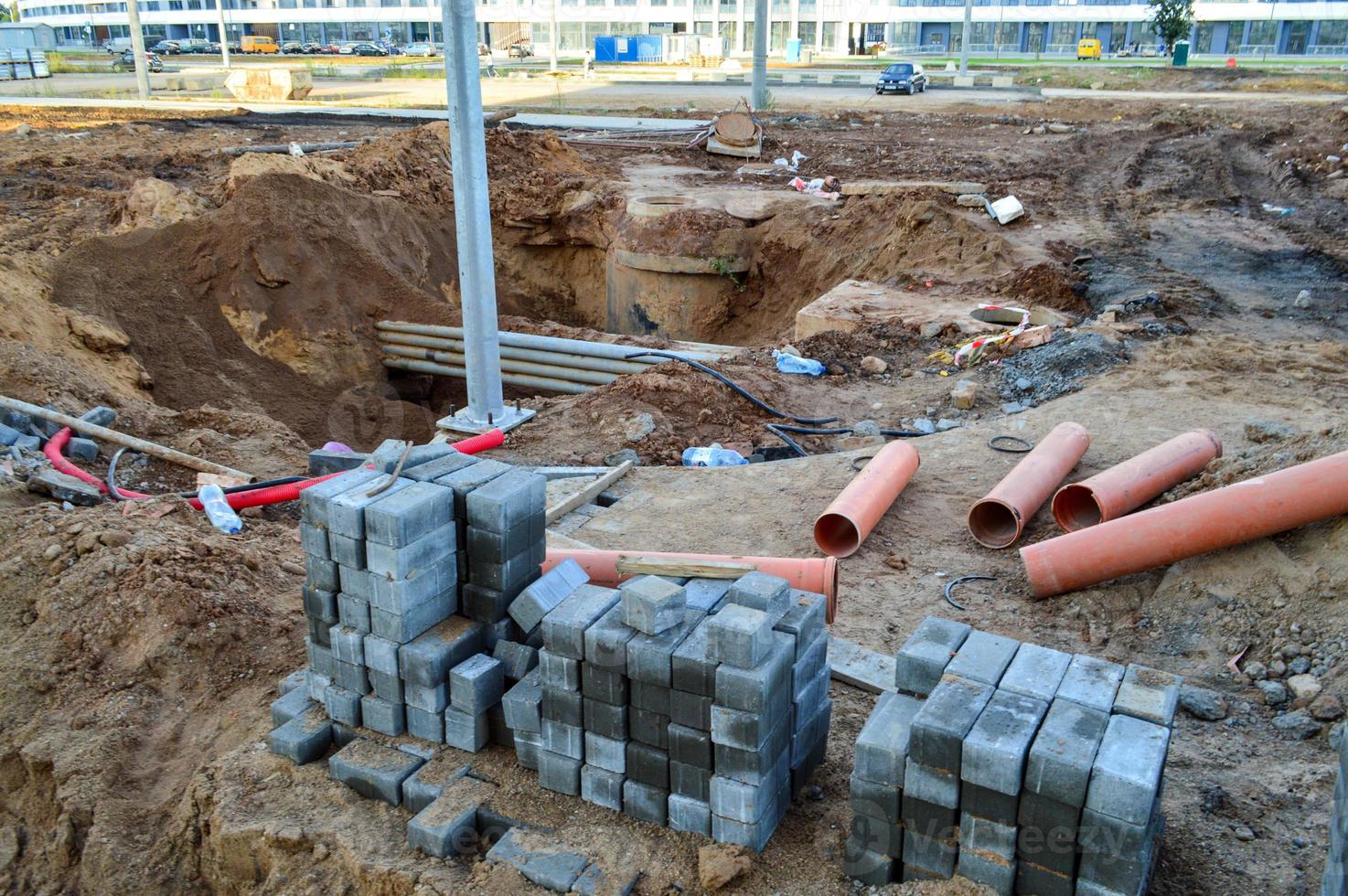 los ladrillos de asfalto yacen en un sitio de construcción. pequeños ladrillos grises se apilan planos en un sitio de construcción en el centro de la ciudad. cerca hay tuberías de metal y una zanja de arena. gran sitio de construcción foto