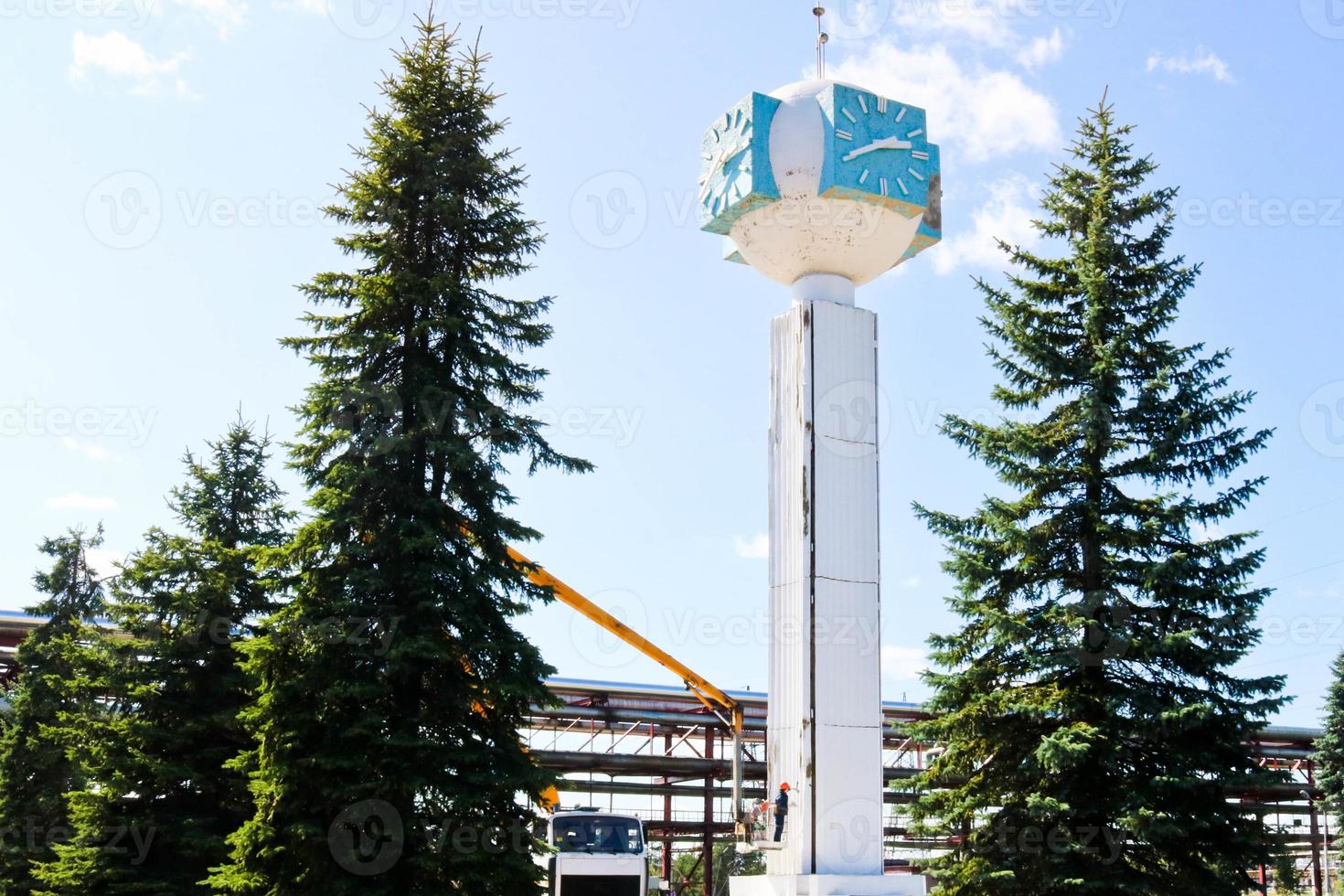Repair of the tower clock. Workers on the crane repair clock-column, clock on the tower, paint, update, perform cosmetic repairs. Unusual clock against the blue sky photo