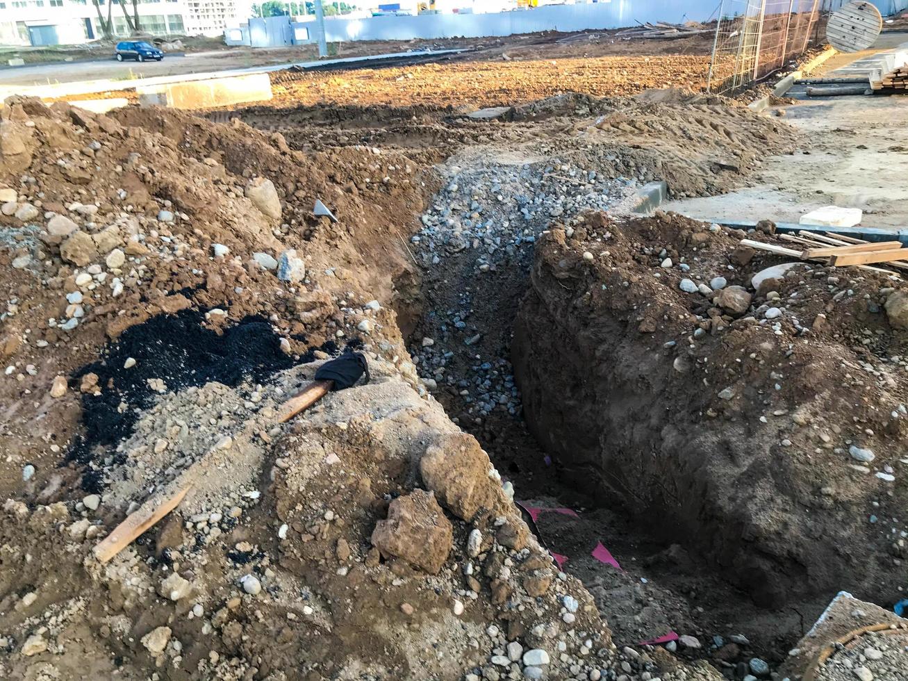 foso de arena en un sitio de construcción. mucha arena, se cavó un hoyo con escombros y piedras. cerca hay escaleras de madera y palos. hay casas nuevas cerca, las comunicaciones se establecerán en el pozo foto