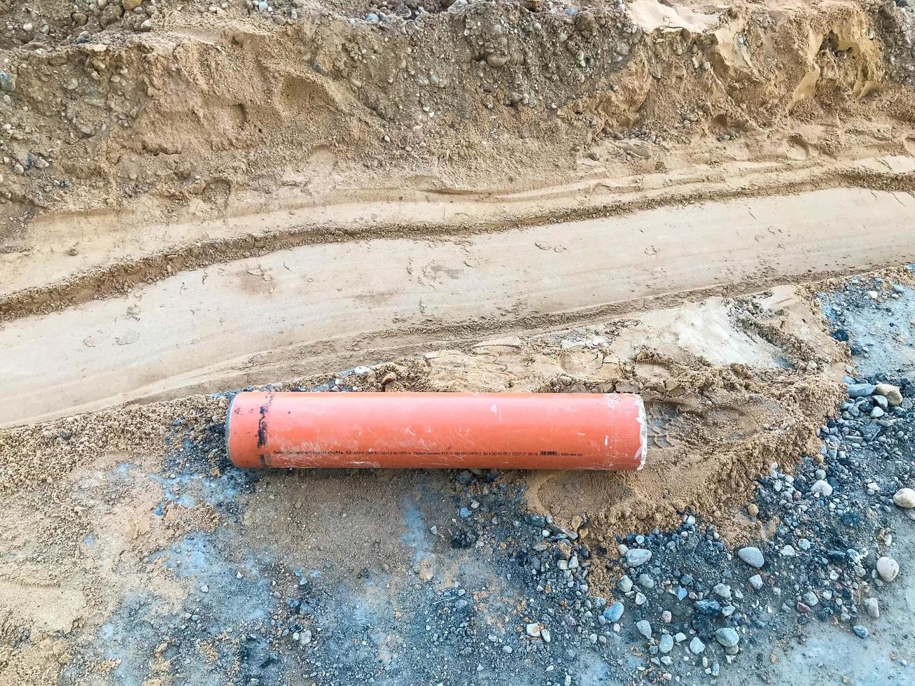 palo de naranja de metal ovalado se encuentra en la arena. la estructura metálica se desprendió del equipo de construcción. la pieza de repuesto se encuentra en el sitio de construcción. la suciedad y las piedras yacen en el suelo foto