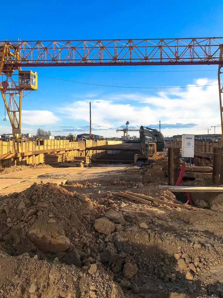 gantry crane to create a metro in the city center. the crane works in the ground, digs long paths. people build a road and rails for high-speed trains. against the blue blue sky photo