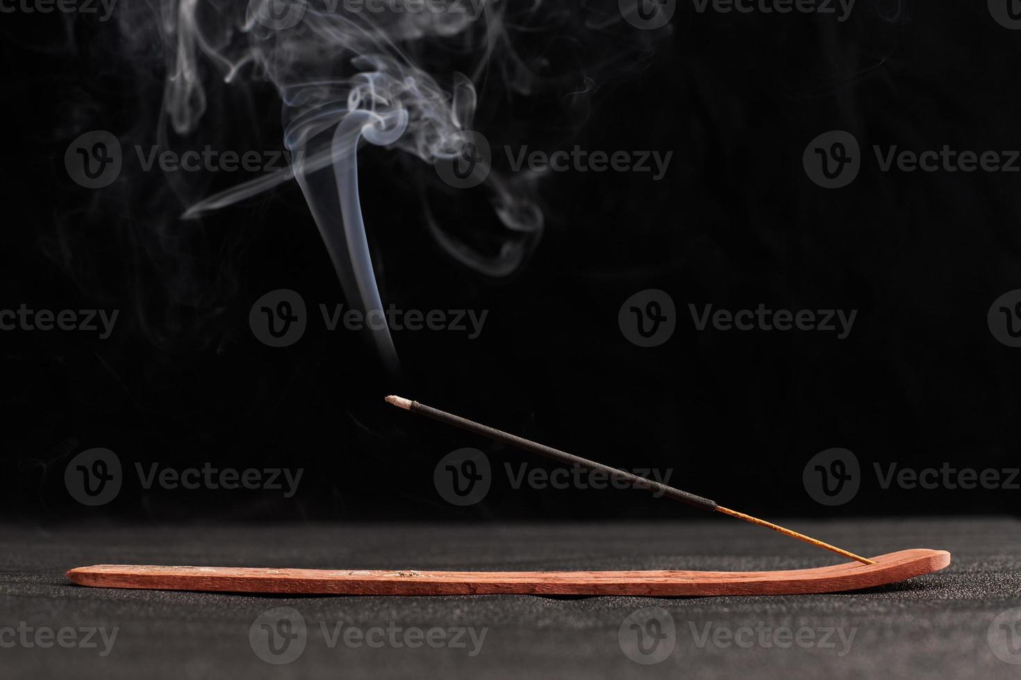 Smoke curls of burning incense stick in wooden holder for relaxation and meditation black background photo