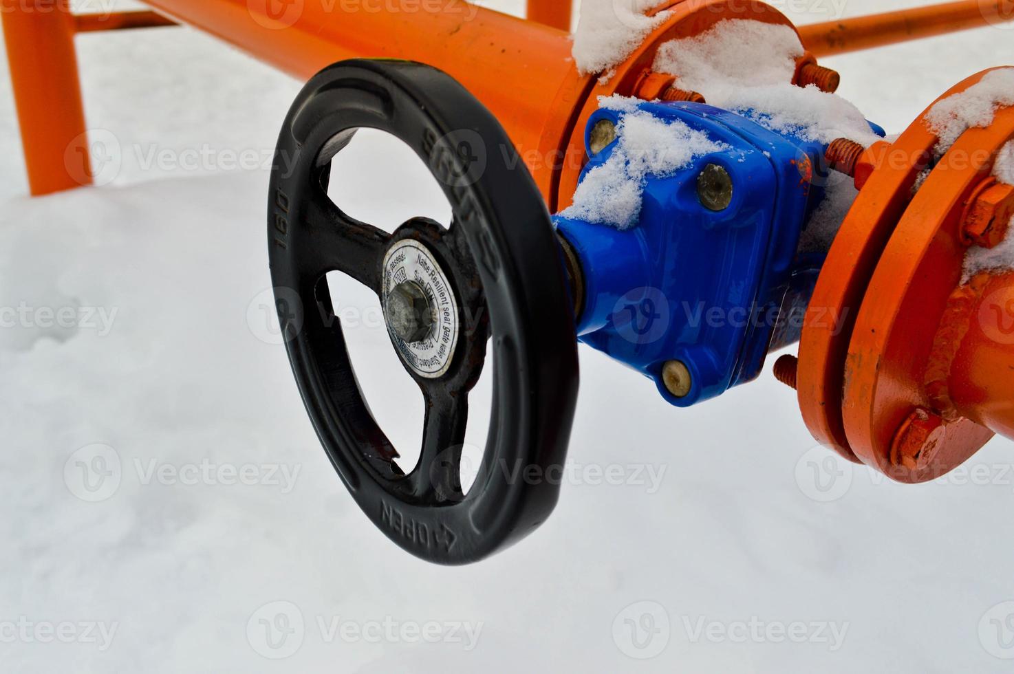 Industrial shut-off regulating protective pipe fittings. Black valve for opening, closing on an iron orange metal pipe with flanges, studs, nuts against the background of white snow in winter photo