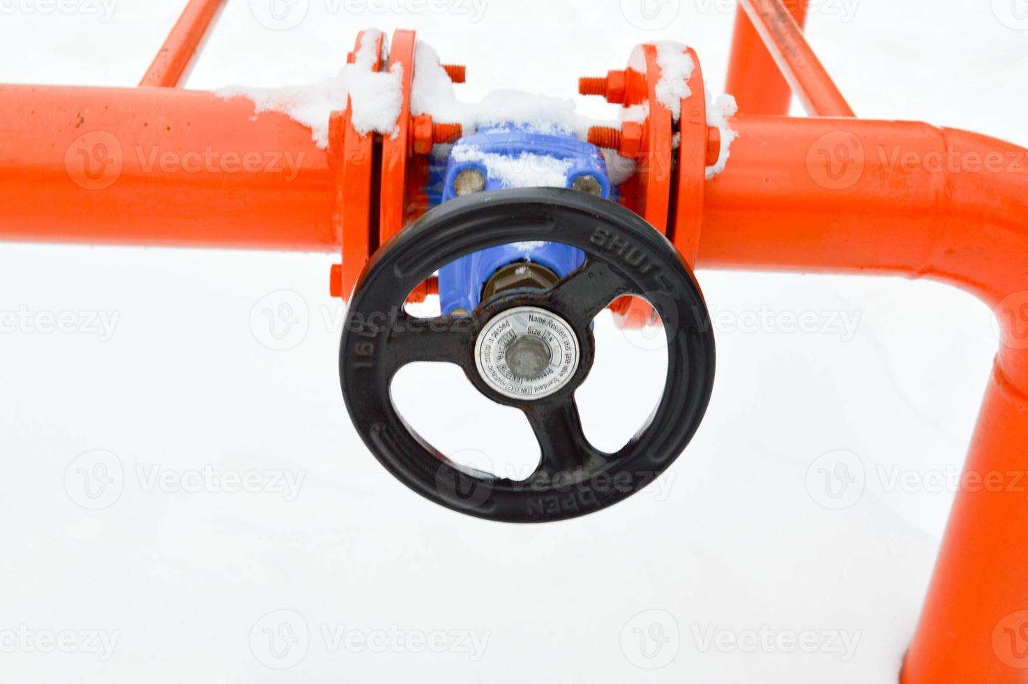 Industrial shut-off regulating protective pipe fittings. Black valve for opening, closing on an iron orange metal pipe with flanges, studs, nuts against the background of white snow in winter photo