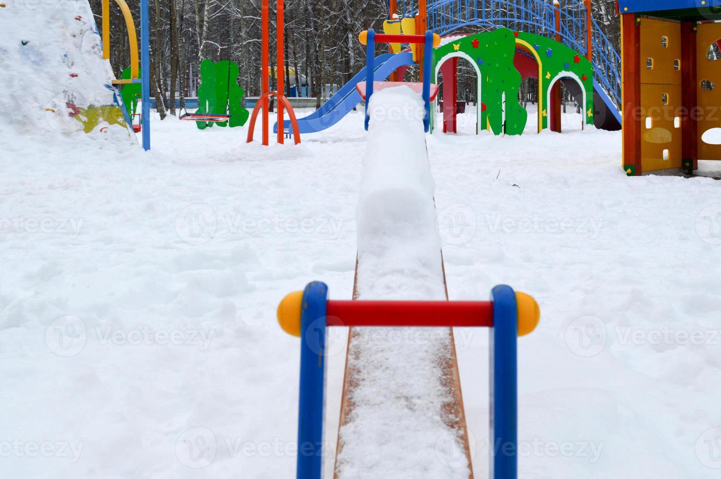 Children's small toy swing balancer covered with snow on a children's playground in the winter photo