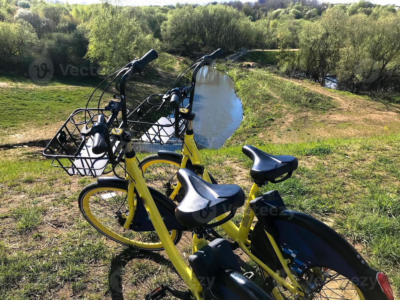 two yellow bicycles stand on the river bank. skiing in the city, in nature, watching the water and swimming. healthy lifestyle, bike in the fresh air photo